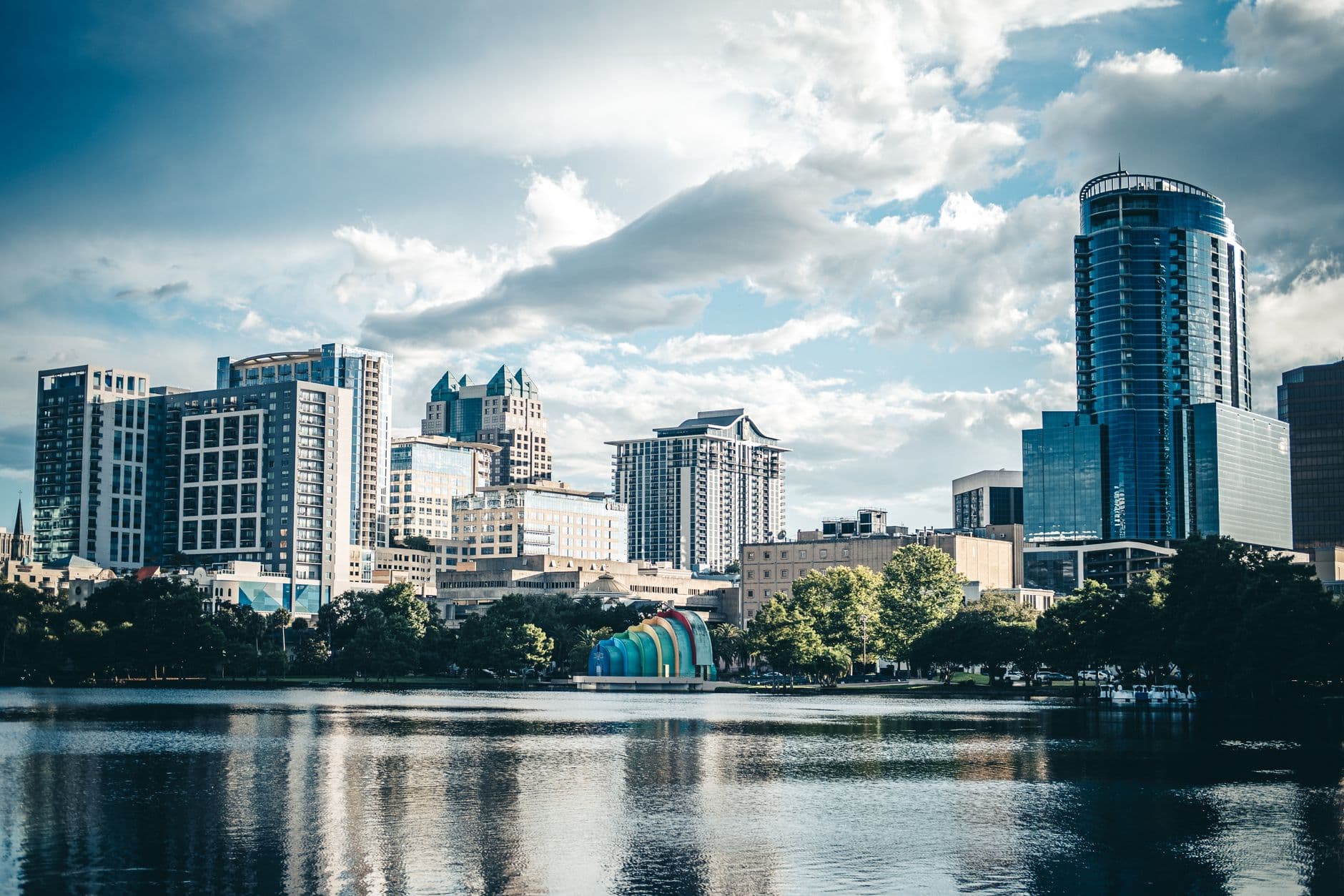 Beautiful city skyline reflected on a serene lake, showcasing modern architecture under a cloudy sky.